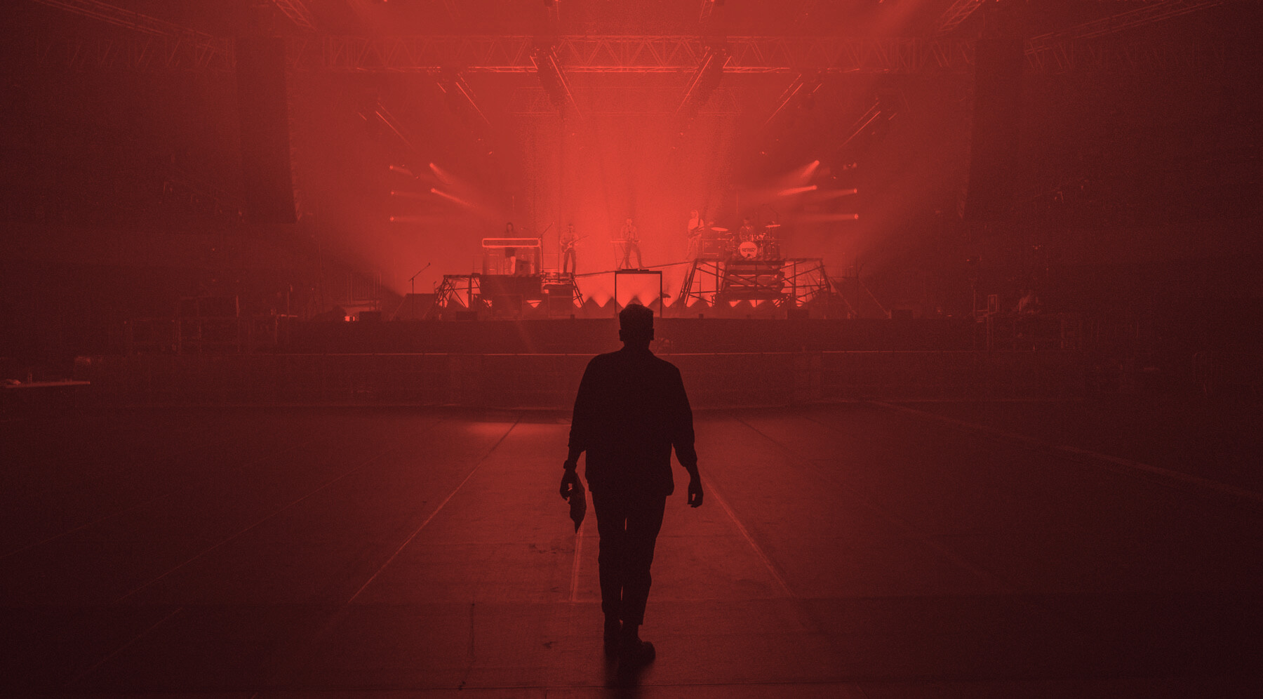 A performer silhouetted before a red-lit stage in a touring arena